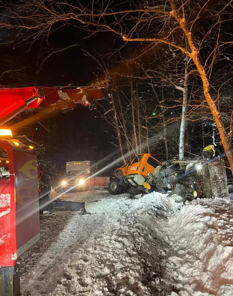 Citywide wrecker recovering an overturned highway department plow truck at night in winter
